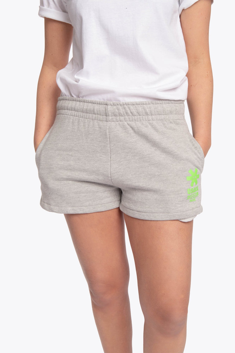 Woman wearing the Osaka women shorts in grey with neon green logo. Front view