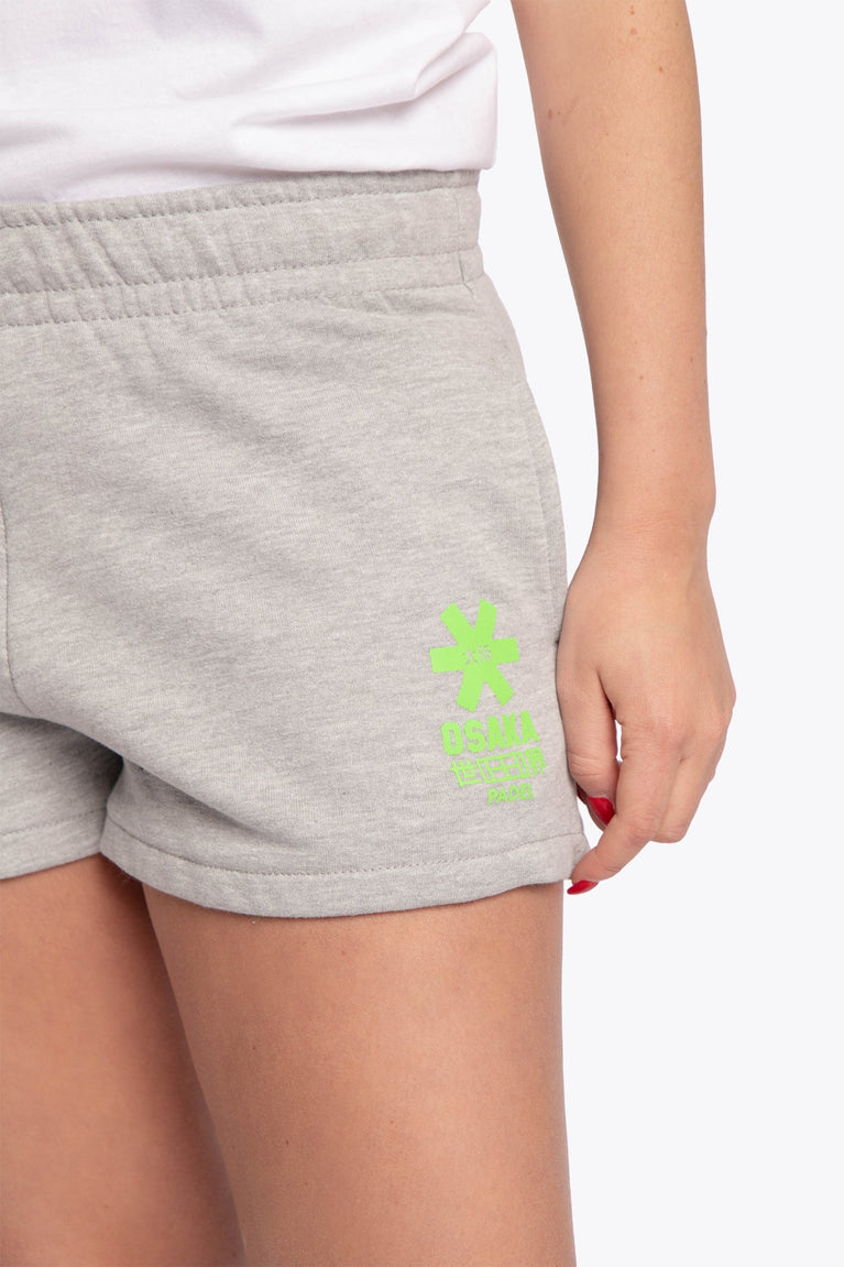 Woman wearing the Osaka women shorts in grey with neon green logo. Front detail logo view