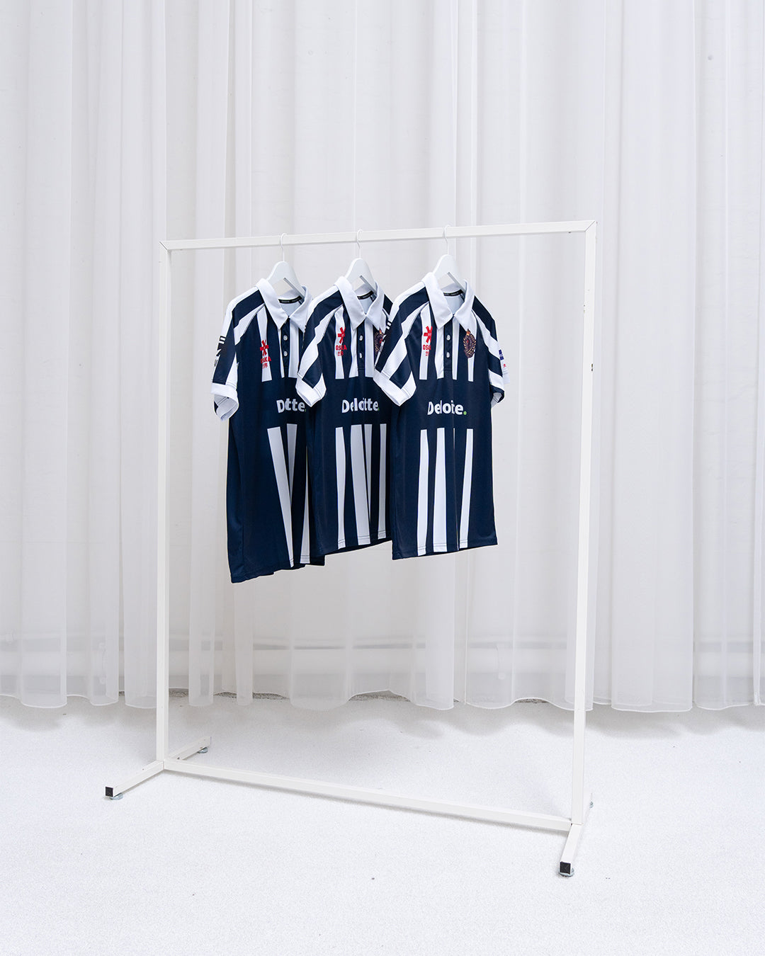Three Osaka custom navy and white striped sports jerseys with sponsor logo and club badge hanging on a rack — fully customized team kit