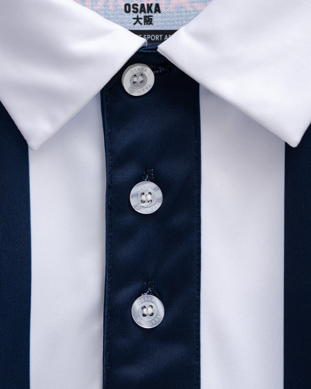 Close-up of Osaka custom teamwear polo collar and branded buttons on a navy and white striped sports jersey — premium kit construction detail