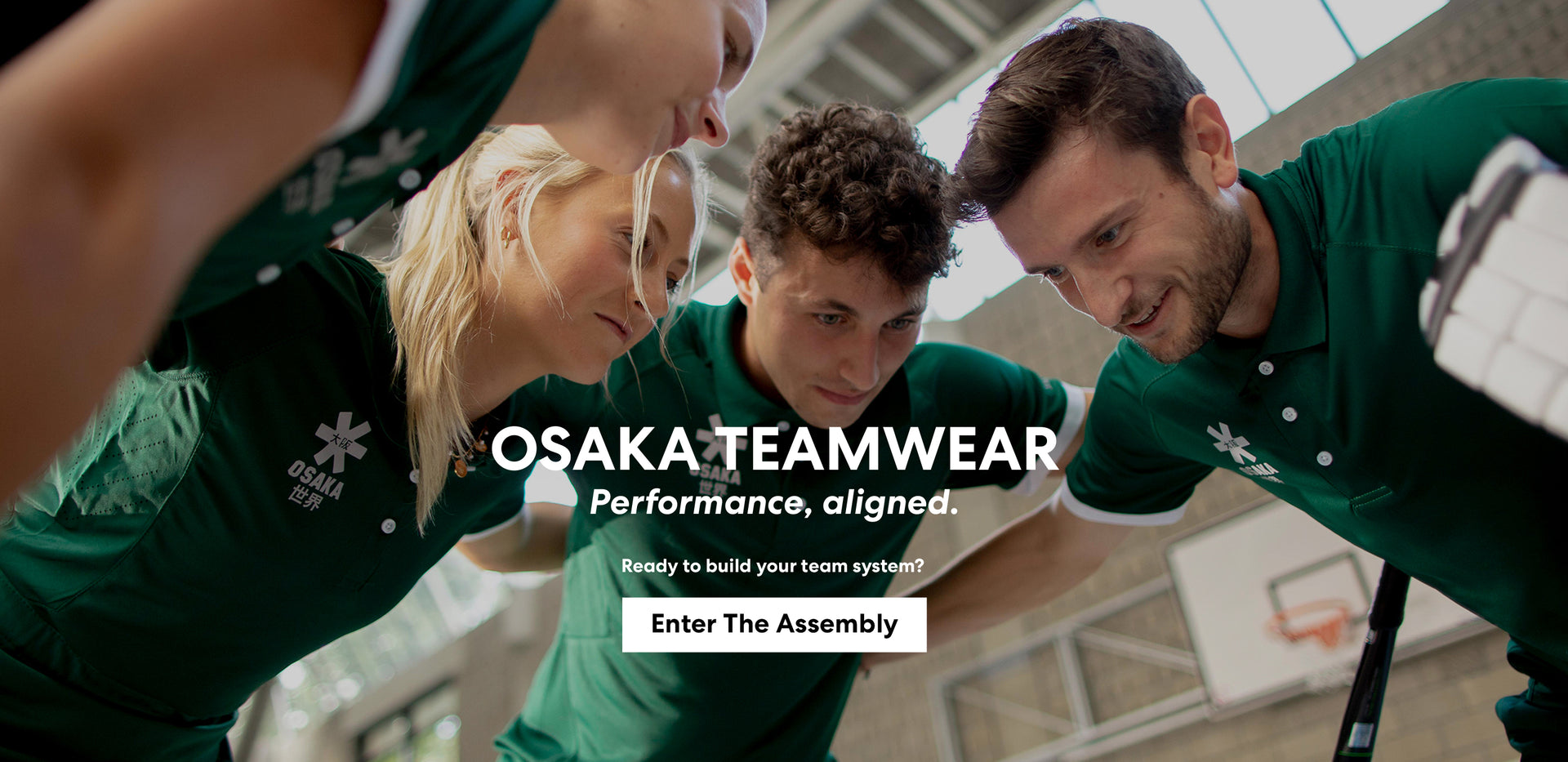 Field hockey team huddle wearing matching Osaka custom green polo teamwear kit inside an indoor sports hall