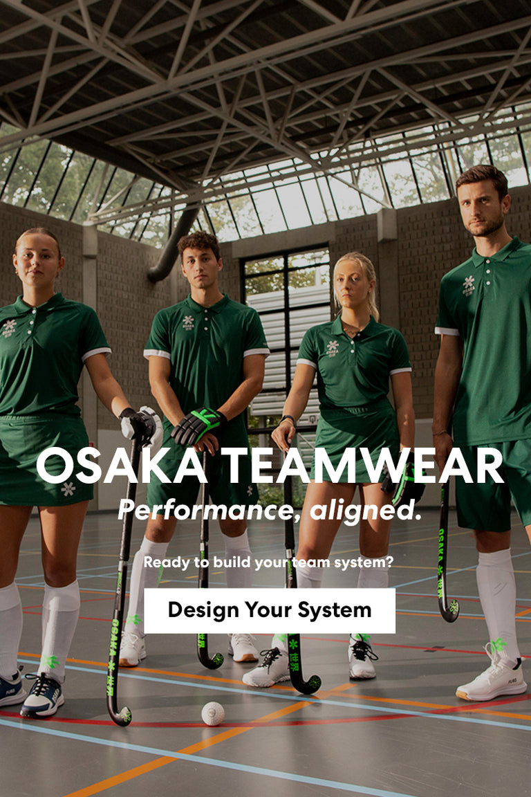 Four field hockey players wearing matching Osaka custom green team kit — polo shirts, shorts, and skort — holding hockey sticks and gloves inside an indoor sports hall