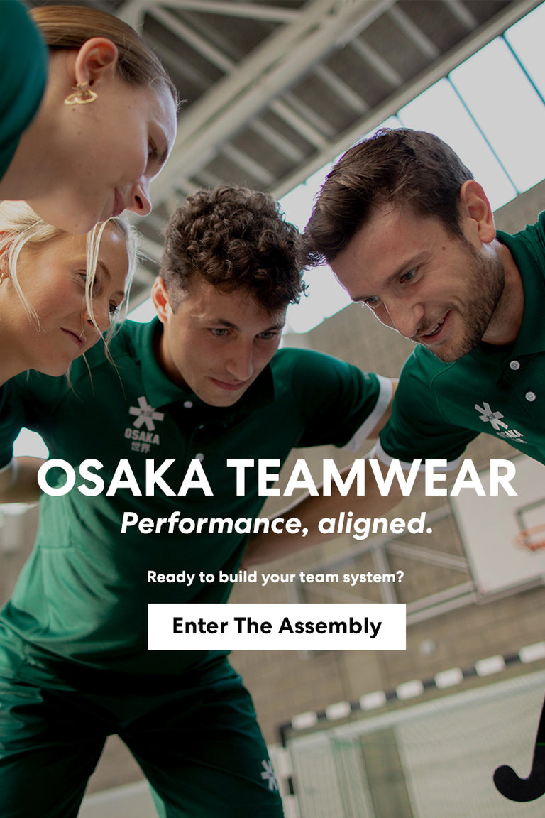 Field hockey team huddle wearing matching Osaka custom green polo teamwear kit inside an indoor sports hall