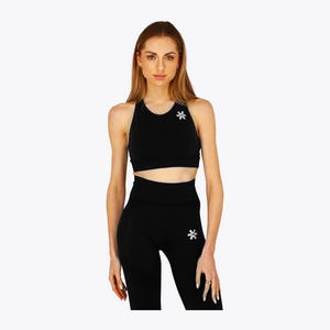 A woman modeling a matching black activewear set consisting of a sports bra and high-waisted leggings, both featuring a small white snowflake logo on the chest and upper thigh, against a plain light gray background. #FadedBlack