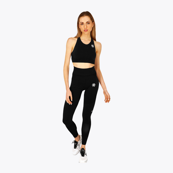 A woman modeling a matching black activewear set consisting of a sports bra and high-waisted leggings, both featuring a small white snowflake logo, set against a plain light gray background. #FadedBlack