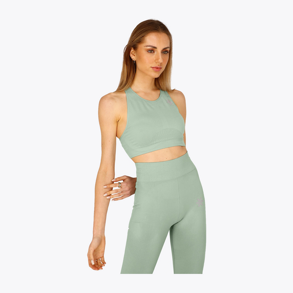A woman modeling a matching sage green activewear set consisting of a sleeveless crop top and high-waisted leggings, set against a plain light gray background. #Jadeite