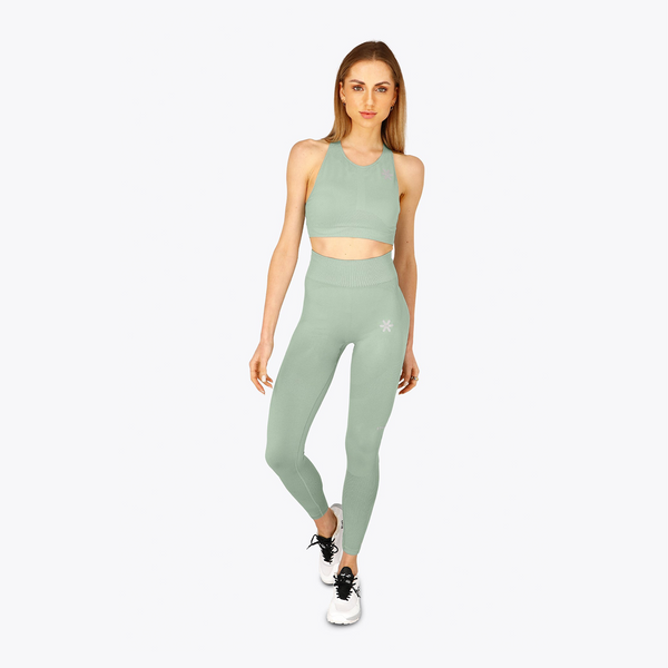 A woman modeling a matching sage green activewear set consisting of a high-neck crop top and high-waisted leggings, paired with white sneakers, against a plain light gray background. #Jadeite