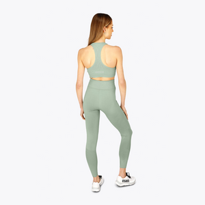 A woman is shown from the back wearing a sage green athletic crop top and matching high-waisted leggings, paired with white sneakers, against a light gray studio background. #Jadeite