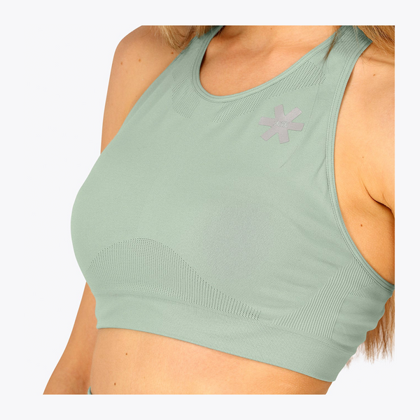 A close-up of a woman wearing a sage green athletic sports bra with a textured star logo on the chest, set against a plain white background. #Jadeite