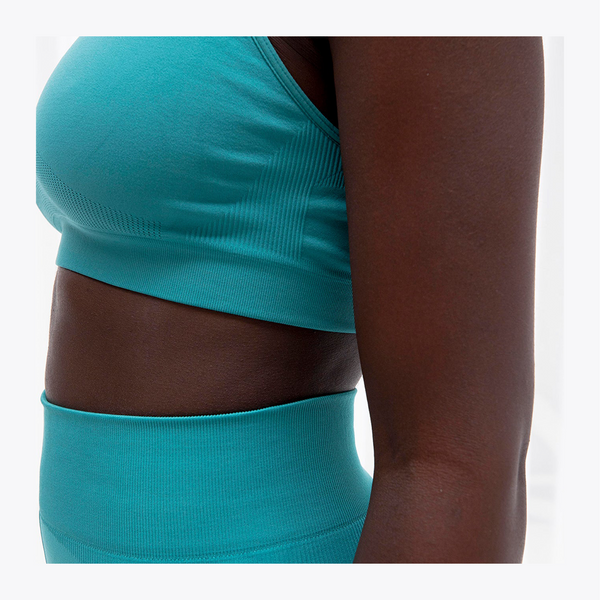 Close-up of a model wearing a matching turquoise ribbed sports bra and high-waisted leggings set, showing the side profile against a plain white background. #BayouGreen