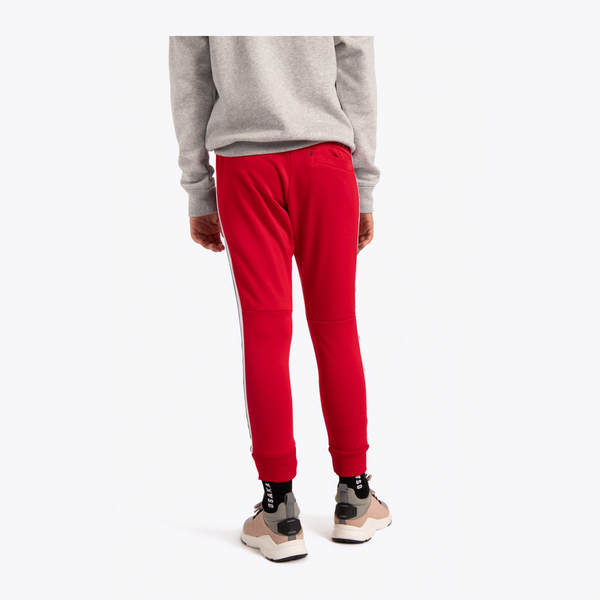 A person shown from the back wearing bright red sweatpants with a white side stripe, a light gray sweatshirt, and beige sneakers against a clean white studio background.