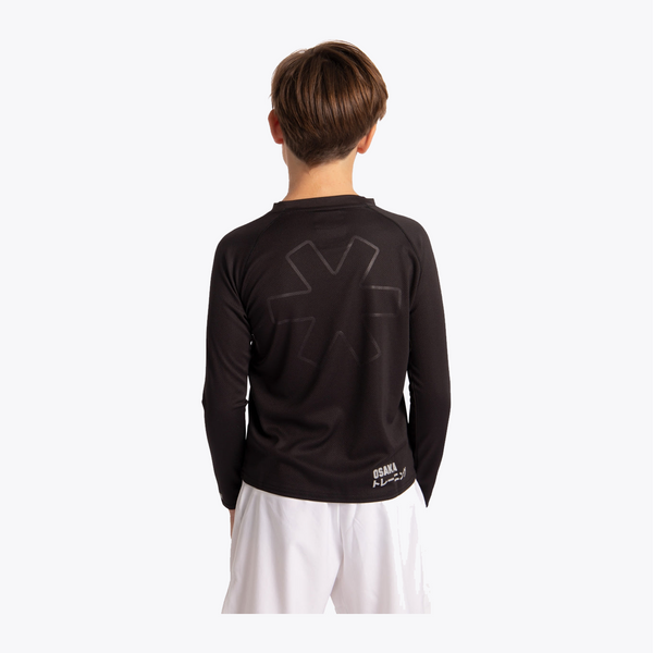 A child viewed from the back wearing a black long-sleeve rash guard with a subtle tonal graphic on the back and a small white brand logo near the hem, paired with white shorts against a light gray studio background. #Black