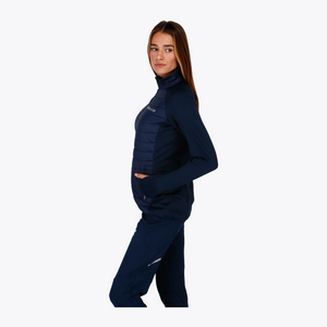 A woman modeling a dark navy blue athletic tracksuit, featuring a long-sleeve mock-neck top with quilted side panels and matching pants, set against a plain white background. #Navy