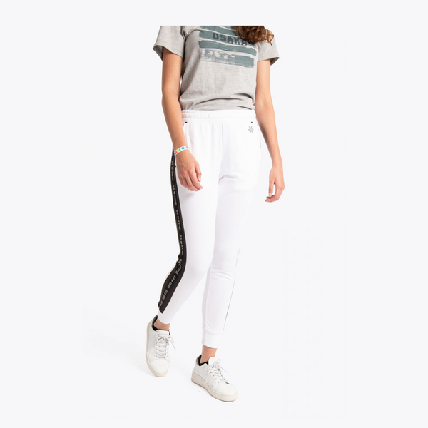 A model wearing white jogger-style pants with a black side stripe featuring white lettering, paired with a gray graphic t-shirt and white sneakers, against a plain white background. #White