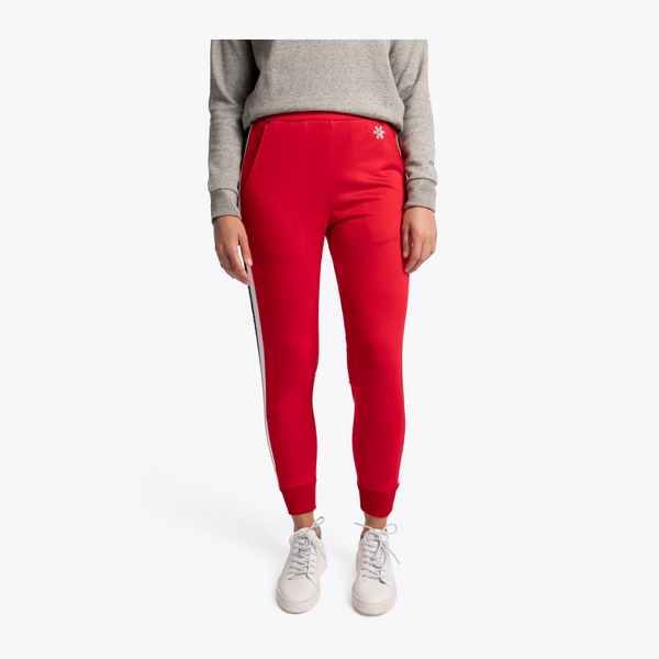 A model wearing bright red jogger-style pants with a white side stripe and a small white star logo on the hip, paired with a gray sweatshirt and white sneakers, against a plain light gray background. #Red
