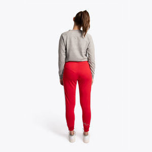 A woman is shown from behind wearing a gray cropped sweatshirt and bright red athletic jogger pants with white stripes down the sides, standing against a plain white studio background. #Red