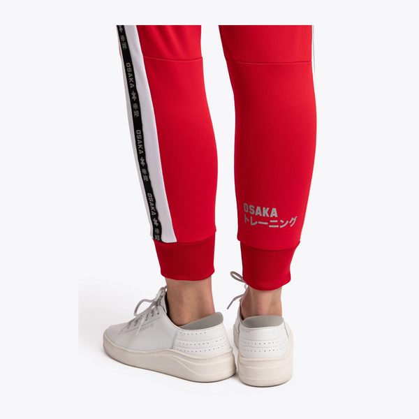 Red athletic jogger pants with white and black side stripes, featuring 'OSAKA TRAINING' text near the ankle, shown on a model from the back wearing white sneakers against a light gray background. #Red