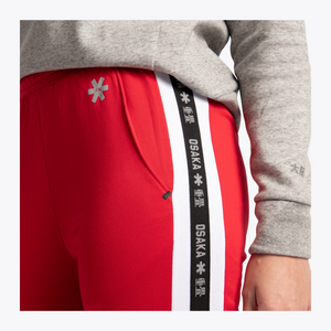 Close-up of a person wearing bright red athletic pants with a wide black-and-white side stripe printed with 'OSAKA' and white snowflake motifs, paired with a heather gray sweatshirt. #Red