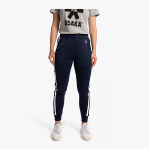 A model wearing navy blue track pants with white side stripes, a gray graphic t-shirt, and white sneakers, shown against a plain light gray background. #Navy