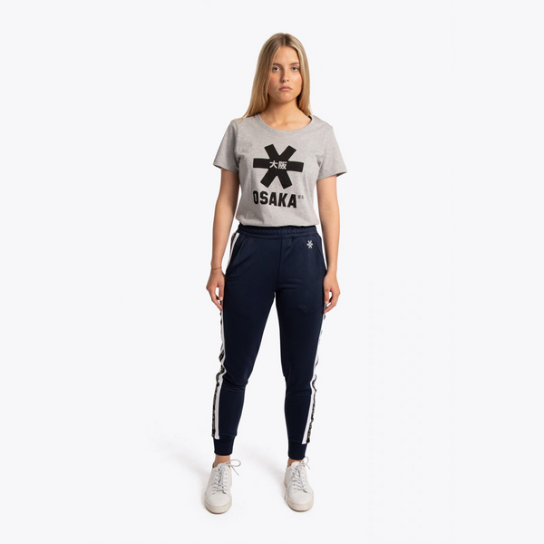 A woman modeling a light gray t-shirt with a black Osaka logo and navy blue jogger pants with white side stripes, paired with white sneakers, against a plain white background. #Navy