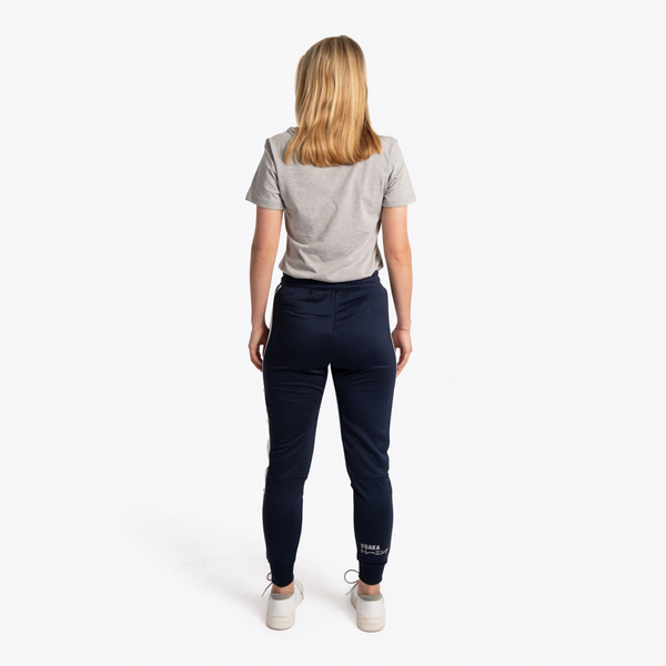 A woman viewed from behind wearing a light gray t-shirt, navy blue pants, and white sneakers against a plain white studio background. #Navy
