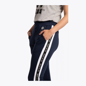 A person wearing navy blue athletic pants with a wide white side stripe featuring repeated black text, paired with a light gray cropped T-shirt, against a plain light background. #Navy