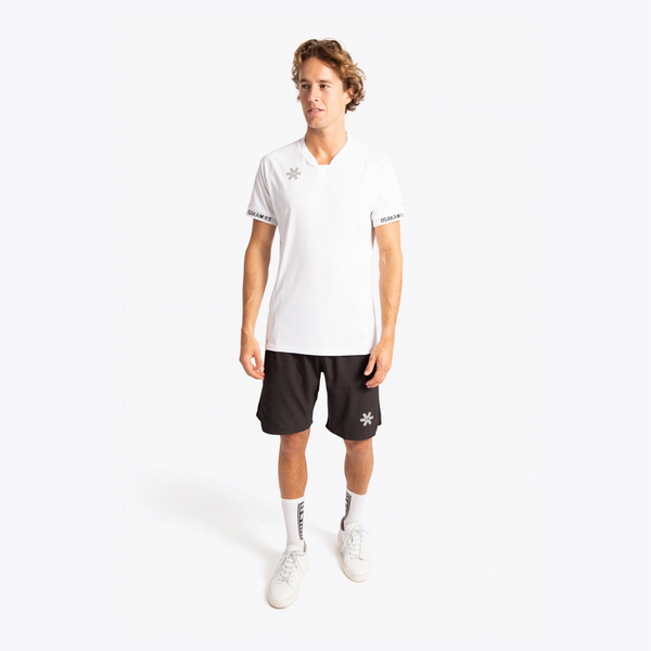 A male model stands against a light gray studio background wearing a white short-sleeve athletic polo shirt with a small star logo on the chest and sleeve trim, black athletic shorts with a small star logo, white socks, and white sneakers. #White