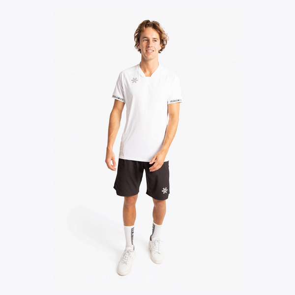 A man modeling a white short-sleeve athletic polo shirt and black athletic shorts with white socks and white sneakers, standing against a plain white studio background. #White
