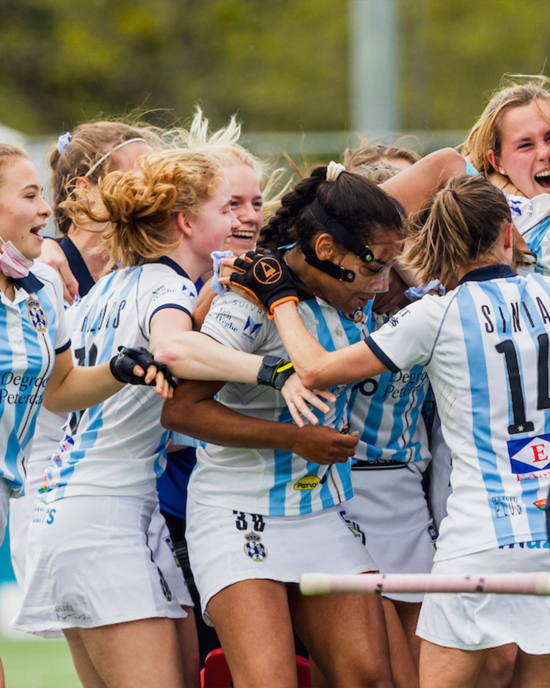 Women's field hockey club team celebrating in Osaka custom white and light blue striped match kit with player numbers, sponsor logos, and club badge
